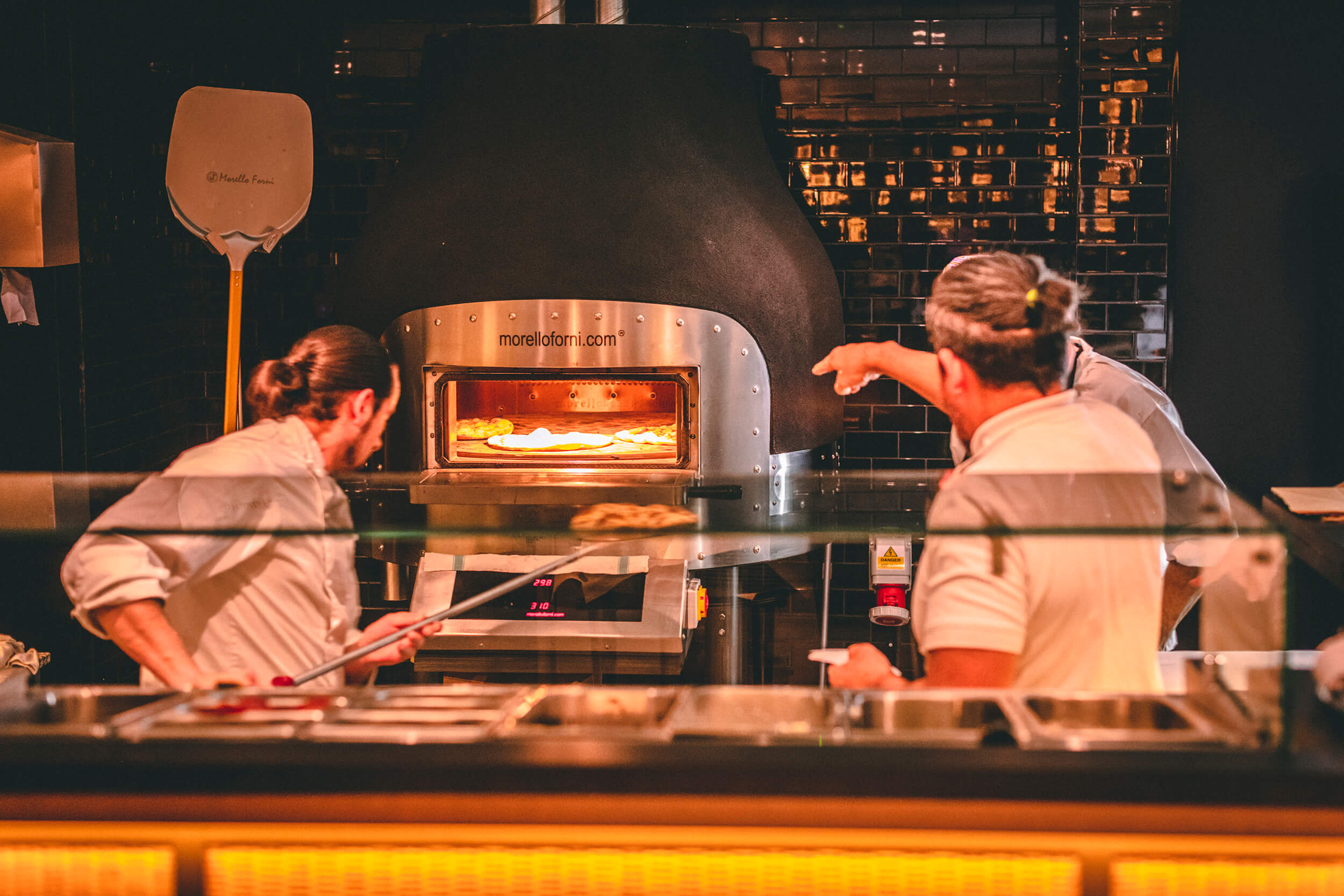 Pizza chefs putting pizza into pizza oven.